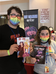 a photo of Anna and one of the writers of Slice of Life, holding up Slice of Life and Dancer. They're both wearing rainbow masks.