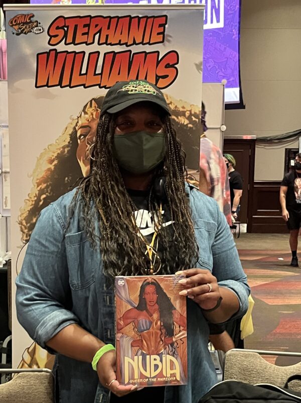 a photo of Stephanie Brown wearing a green mask holding the Nubia book